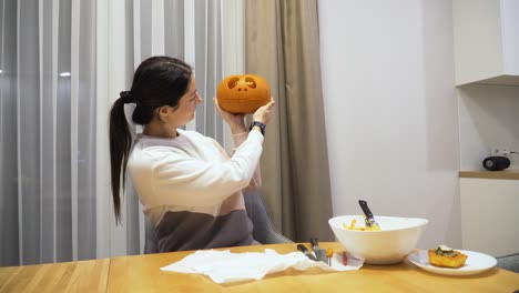 shot-of-a-young-woman-at-home-showing-a-carved-pumpkin-for-the-Halloween-decoration