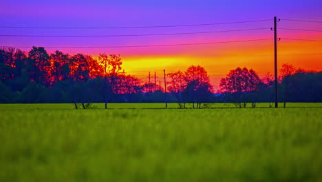 Slow-Zoom-Out-Across-Green-Field-With-Dramatic-Purple-Red-Orange-Sunset-Sky