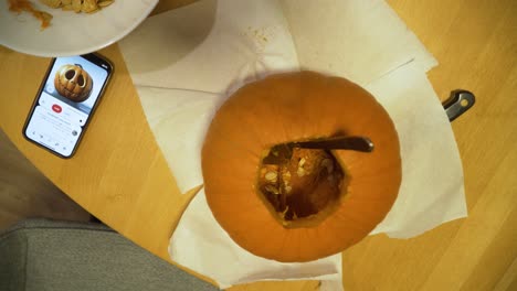 top-down-shot-of-pumpkin-ant-phone-with-a-carved-pumpkin-picture-on-the-table,-pumpkin-in-the-carving-process-for-Halloween