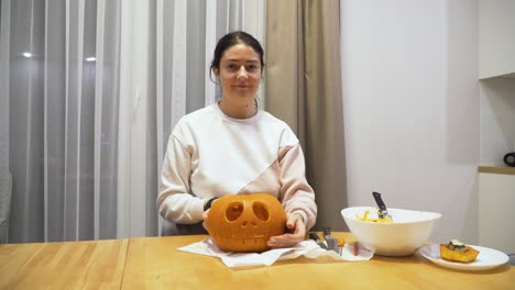 shot-of-a-young-woman-at-home-showing-a-carved-pumpkin-for-the-Halloween