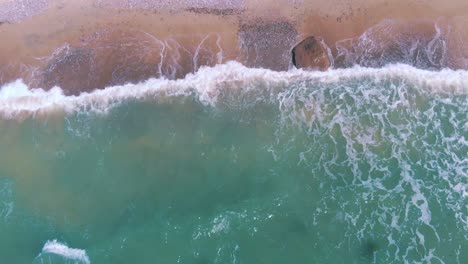Top-down-aerial-view-of-tropical-beach-with-waves-crashing-against-shore