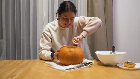 Foto-De-Una-Mujer-Joven-Tallando-Calabaza-Naranja-En-Casa-Para-Halloween