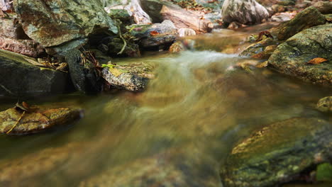 Babbling-brook-flowing-along-a-rocky-creek-bed-in-autumn---long-exposure-time-lapse