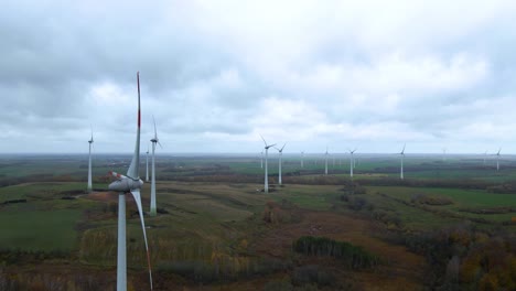 Aerial-orbit-shot-of-multiple-spinning-wind-turbines-for-renewable-electric-power-production-in-a-wide-rural-area-on-a-cloudy-day