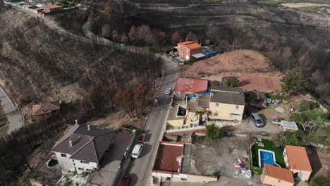 Aerial-bird's-view-of-car-entering-village-surrounded-by-burnt-forest,-forward