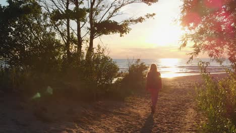 Woman-walking-towards-sunset-over-Baltic-sea,-back-follow-view