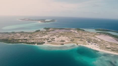 Aerial-view-tropical-island-surrounded-shades-of-blue-sea-water-and-coral-reef,-Los-Roques