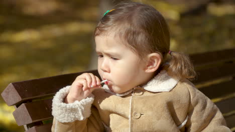 Young-Girl-Licking-Lollipop-Outdoors-in-Public-Park-in-Autumn---Portrait