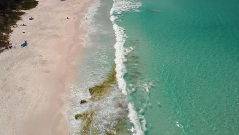 Aerial-view-over-people-in-the-waves,-at-Hyams-Beach-in-Jervis-bay,-NSW,-Australia---tilt,-drone-shot