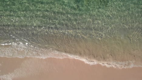 Aerial-view-above-calm,-transparent-sea-water,-waves-and-a-tropical-beach---birds-eye,-drone-shot