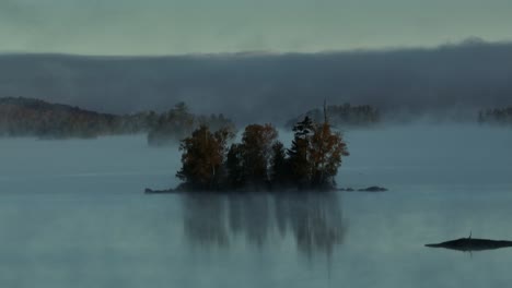 Aerial-view-of-fog-sets-in-around-lone-island-on-lake
