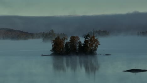 Aerial-view-of-fog-sets-in-around-lone-island-on-lake-Slow-Motion