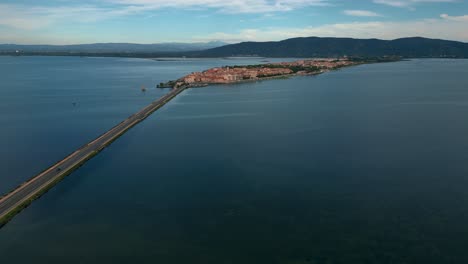 Cars-on-a-bridge-road-toward-the-lagoon-toward-the-old-island-town-Orbetello-close-to-Monte-Argentario-and-the-Maremma-Nature-Park-in-Tuscany,-Italy,-with-water-reflections