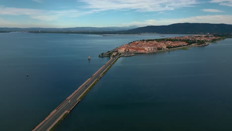 Cars-on-bridge-road-across-the-lagoon-toward-the-island-town-Orbetello-close-to-Monte-Argentario-and-the-Maremma-Nature-Park-in-Tuscany,-Italy,-with-water-reflections