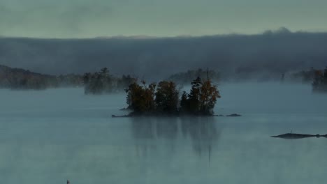 Spectacular-aerial-dawn-fog-surrounds-lake-island-Slow-Motion-Aerial
