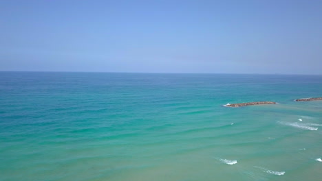 Sunny-Summer-Aerial-in-Israel,-Ashkelon-Beach---Flyby-to-the-Ocean-over-rock-dams