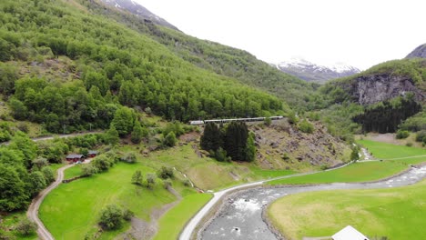 Aerial:-Flåm-train-going-uphill-through-by-a-mountain-side-in-a-valley
