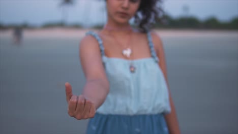 View-of-young-woman-holding-a-shell-in-hand-and-gathering-a-handful,-shallow-focus,-slow-motion