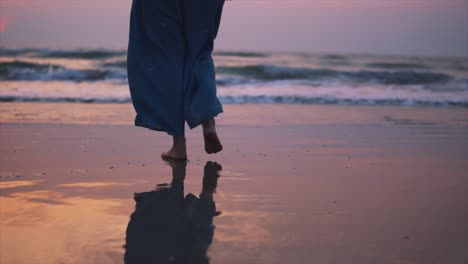 View-of-girl-walking-barefoot-on-a-sandy-beach,-footprints-and-surface-reflection,-sea-waves