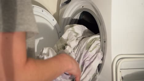 Young-Caucasian-adult-pulls-warm-laundry-bed-sheets-from-clothes-dryer