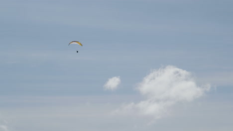 Powered-paraglider-soaring-high-into-blue-sky-with-few-white-clouds,-long-shot