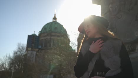 Beautiful-Blonde-Woman-in-Hat-Posing-Outdoors-for-Photoshoot-Against-Bright-Sun-and-Berlin-Cathedral