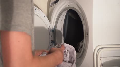 Young-man-loads-clothes-into-white-laundry-dryer,-then-closes-door