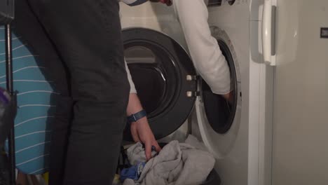 Caucasian-man-pulls-laundry-from-white-front-load-washing-machine