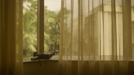 Canon-Super-8mm-Kamera-Auf-Der-Fensterbank-Warmer-Raum,-Goldene-Hitze,-Indien,-Palmen-Im-Hintergrund,-Warme-Durchhänge-Und-Vorhänge-Kamerafotografie-Und-Reisevideo,-Die-Erinnerungen-An-Den-Urlaub-Festhalten