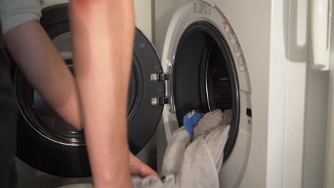 Close-up:-Young-man-empties-washing-machine-into-laundry-basket