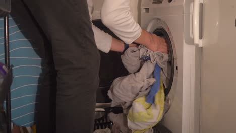 Young-man-brings-laundry-basket-and-stuffs-front-load-washing-machine