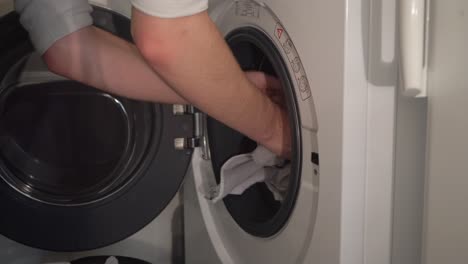 Laundry-close-up:-Man-loads-clothes-into-front-load-washing-machine