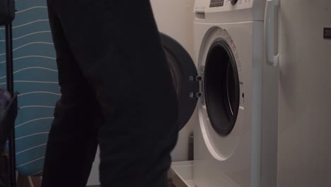 Young-man-picks-up-laundry-basket-from-front-load-washing-machine