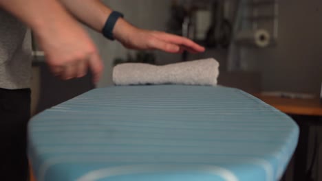 Young-Caucasian-male-folds-laundry-towels-on-ironing-board,-low-angle
