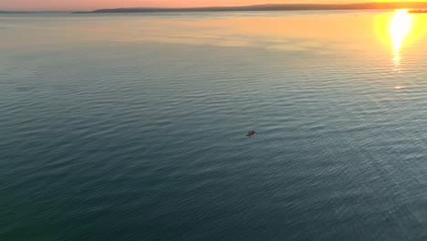 Aerial-drone-view-circling-left-of-two-people-in-sea-kayak-paddling-in-a-bay-near-seattle-washington-at-sunrise-with-sun-glare-reflection-off-water