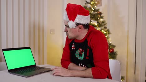 Festive-male-wearing-Santa-hat-and-sweater-looking-at-laptop-computer-green-screen-with-thinking-expressions-wondering-about-what-to-do