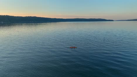 Aerial-drone-view-circling-left-of-two-people-in-sea-kayak-paddling-in-a-bay-near-seattle-washington-at-sunrise-revealing-southworth-community-town