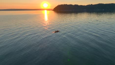 Aerial-drone-view-fly-in-approach-of-young-couple-paddling-off-into-the-sunset-in-a-sea-kayak-in-bay-near-seattle-washington-at-sunrise