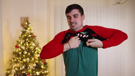Excited-male-putting-on-Christmas-jumper-looking-at-camera-sad-finding-it's-the-wrong-size-fitting,-short-sweater-slow-motion