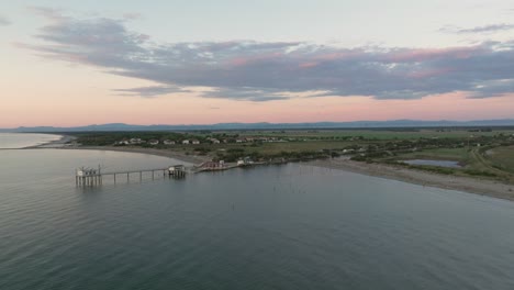 Aerial-view-slow-motion-of-fishing-huts-on-shores-of-estuary-at-sunset,italian-fishing-machine,-called-"trabucco"-Ravenna-near-Comacchio-valley