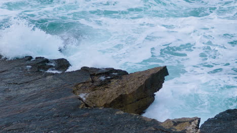 Sea-waves-breaking-on-rocky-shore-creating-foam-and-mist-on-stormy-weather---close-up