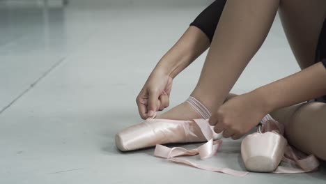 Die-Junge-Ballerina-Bindet-Ihre-Schnürsenkel,-Während-Sie-Auf-Dem-Tanzpodium-Sitzt