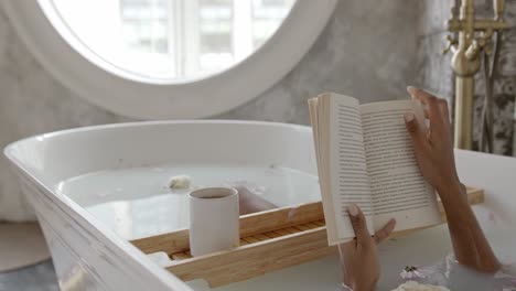 Woman-taking-a-bath-with-flowers-in-the-bathtub-while-having-tea-and-reading-a-book,Concept-of-leisure,-education,-rest,-comfort,-skin-care,-health
