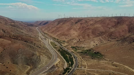 Californian-valley-with-highway,-railway-and-electrical-windmills-producing-clean-energy
