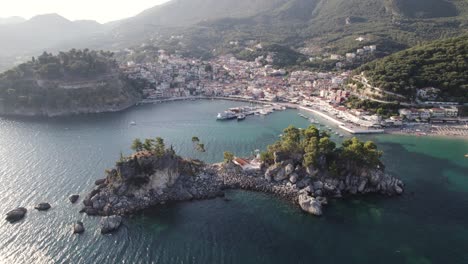 Aerial-view-of-harbor-and-coast-of-tourist-town-Parga-in-Greece,-small-island-and-forest-in-background