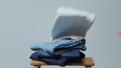 Tirando-Jeans-Doblados-En-Un-Pequeño-Taburete-De-Madera,-Fondo-De-Un-Solo-Color,-Bueno-Para-Superposiciones