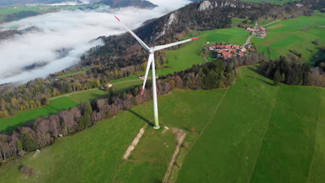 Turbina-Eólica-Girando-En-La-Cima-De-La-Montaña-Jura-Suiza-Con-El-Pueblo-En-El-Fondo-30fps-4k