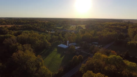 Aerial-shot-of-outdoor-wedding-venue-in-a-rural-location-with-fall-colors,-cinematic-drone-shot-into-the-sun