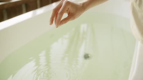 Woman-is-adding-bath-salts-to-the-warm-water-in-the-bath-tube