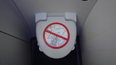 Airplane-onboard-bathroom-toilet-seat-with-lid-closed-and-prohibited-objects-warning-sign-on-it
